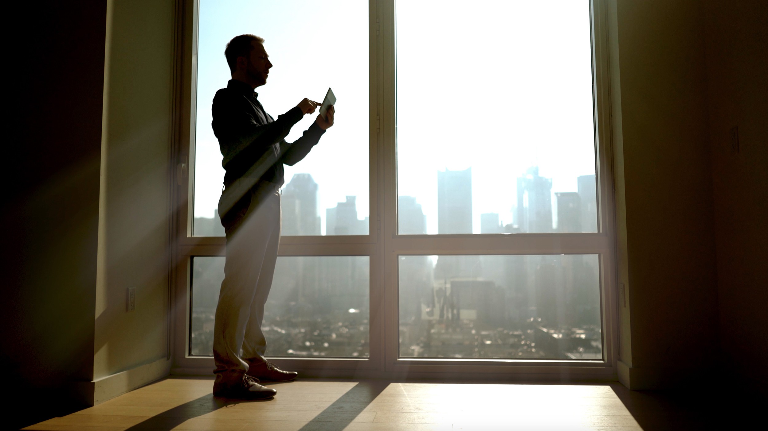 silhouette of man standing on window front looking over the city. businessman working in modern office. sun beaming light and shadow background
