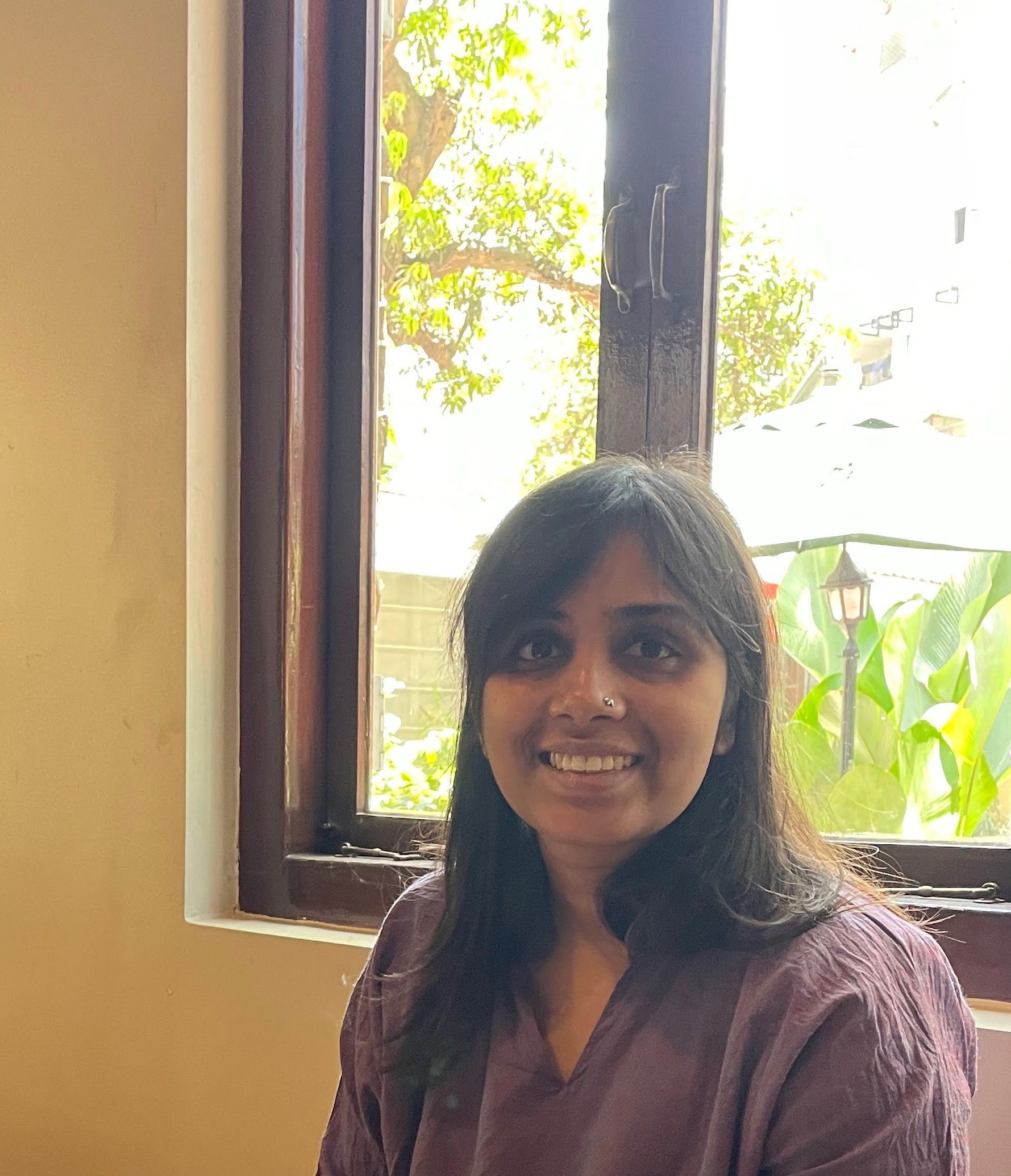 A photo of Prajna Nayak smiling, with a drink in hand. There's a cafe in the backdrop, and people sitting at tables.