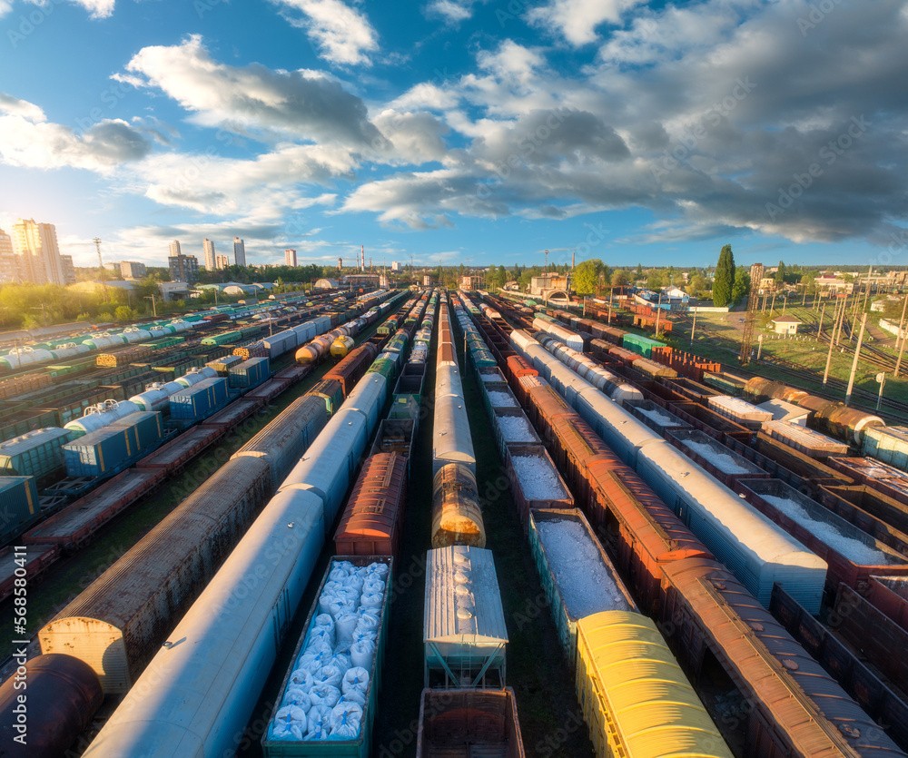 Aerial view of freight trains on interconnected rail tracks with a logistics hub in the background, symbolizing freight modernization.