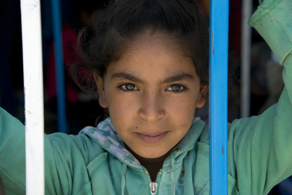 Young girl looking out through the blue bars of a window