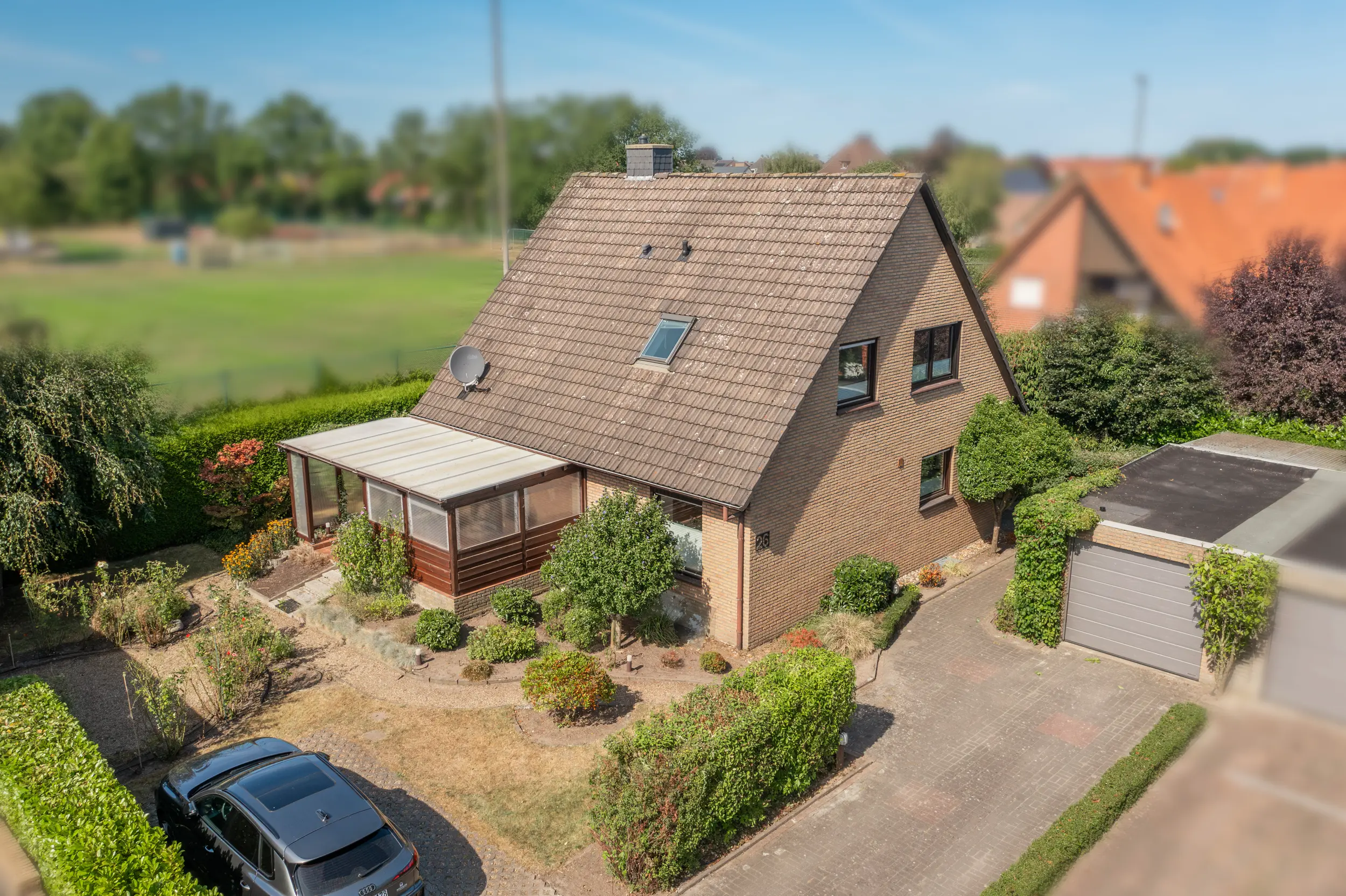 Schräge Luftaufnahme der Gartenseite mit Wintergarten und Garage; die Umgebung ist weichgezeichnet.