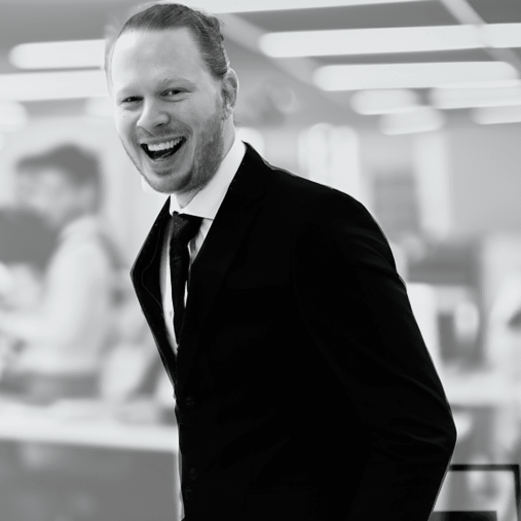 A smiling young woman in a pink blouse stands in an office setting, with soft lighting and a professional backdrop.