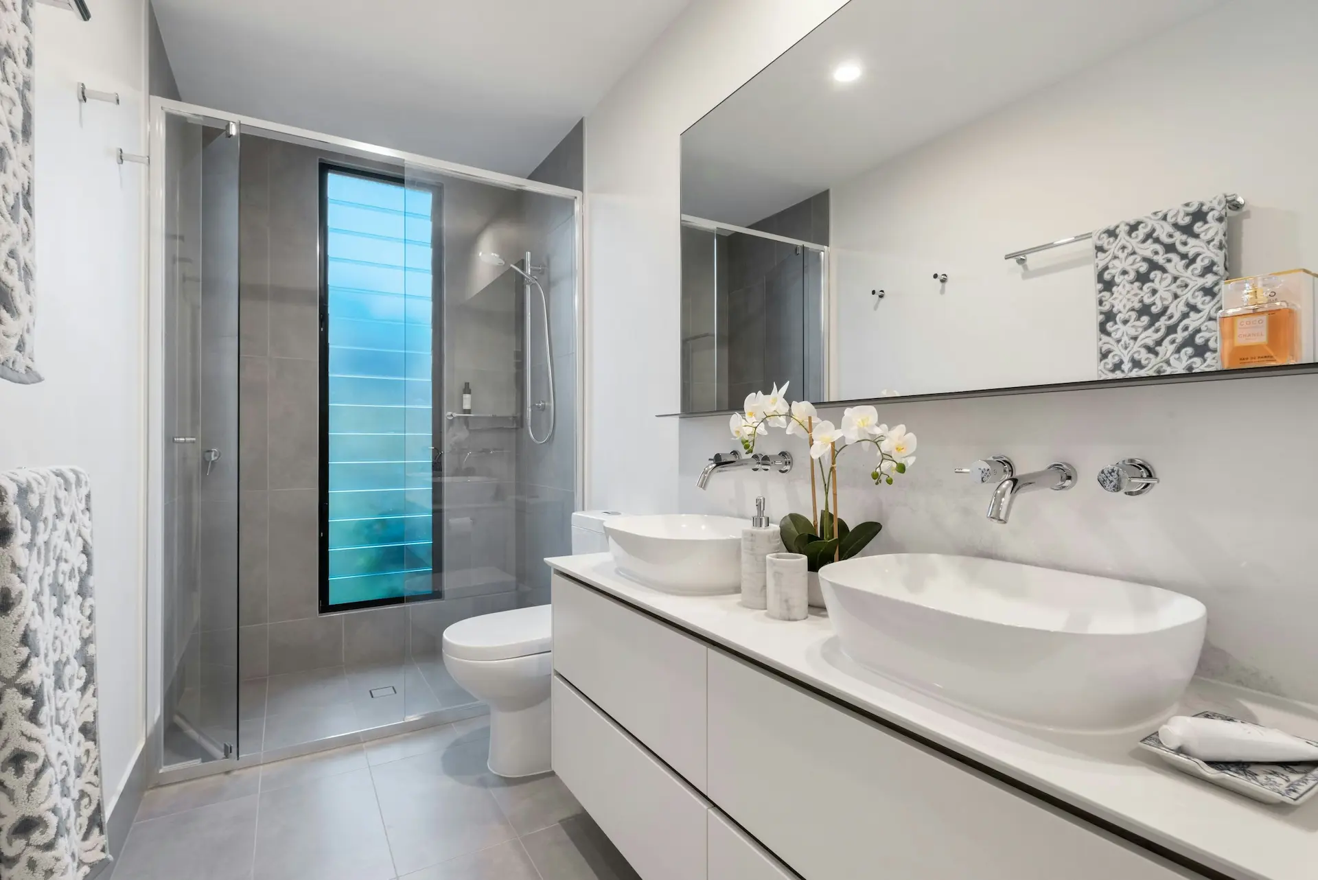 Deep cleaned modern bathroom with sparkling white double vanity sinks and a spotless glass shower door.