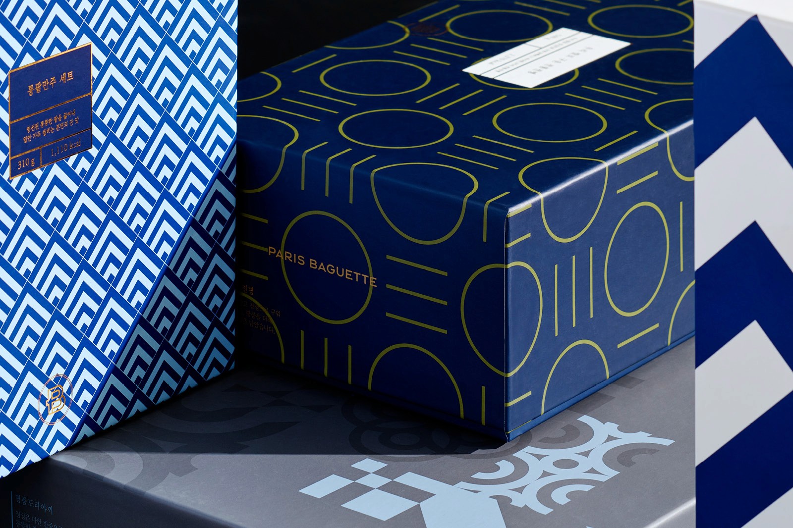 Two blue boxes with geometric patterns and a white label, placed on a textured surface with a zigzag design.