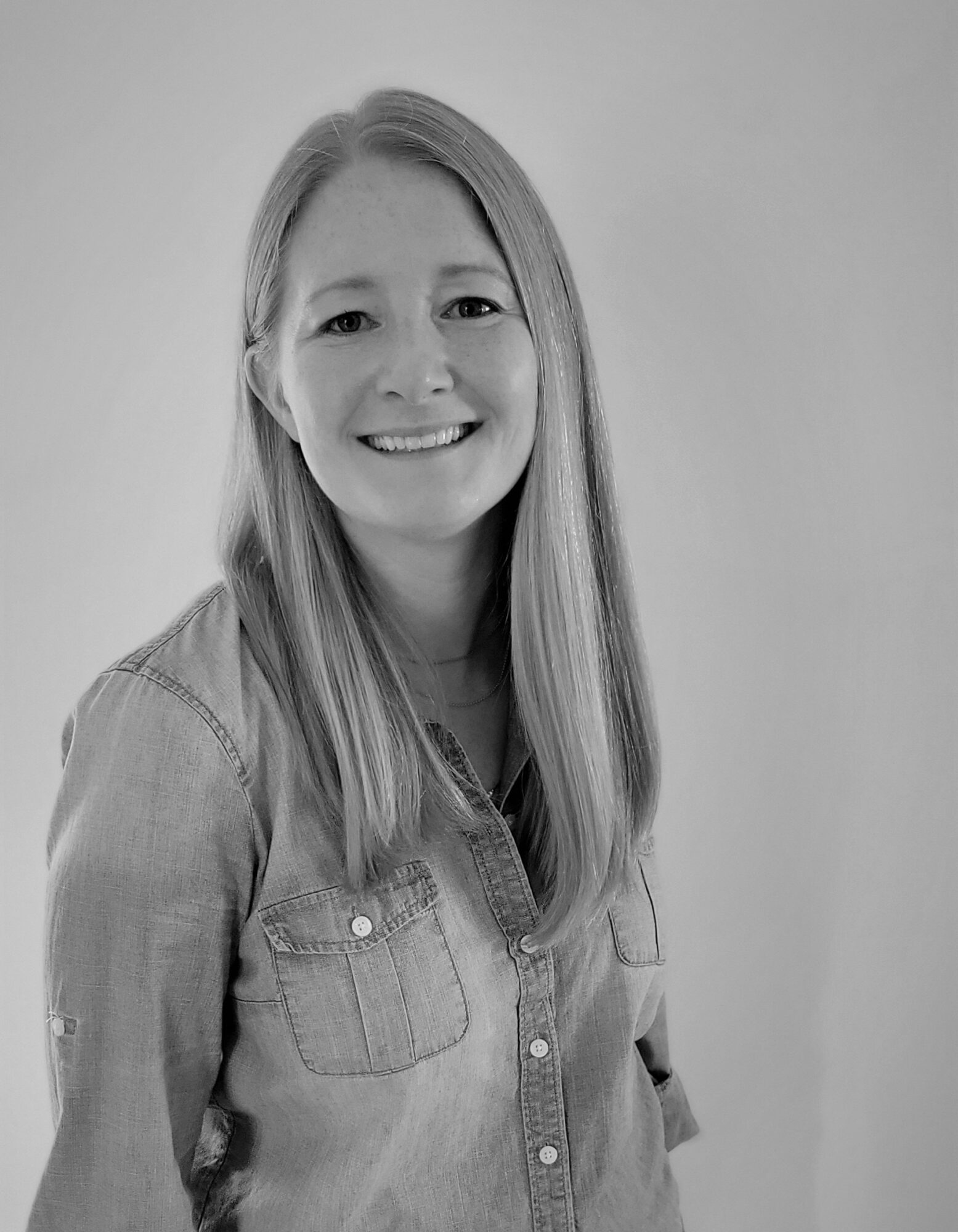A smiling woman with long hair wearing a light shirt, posed against a neutral background.