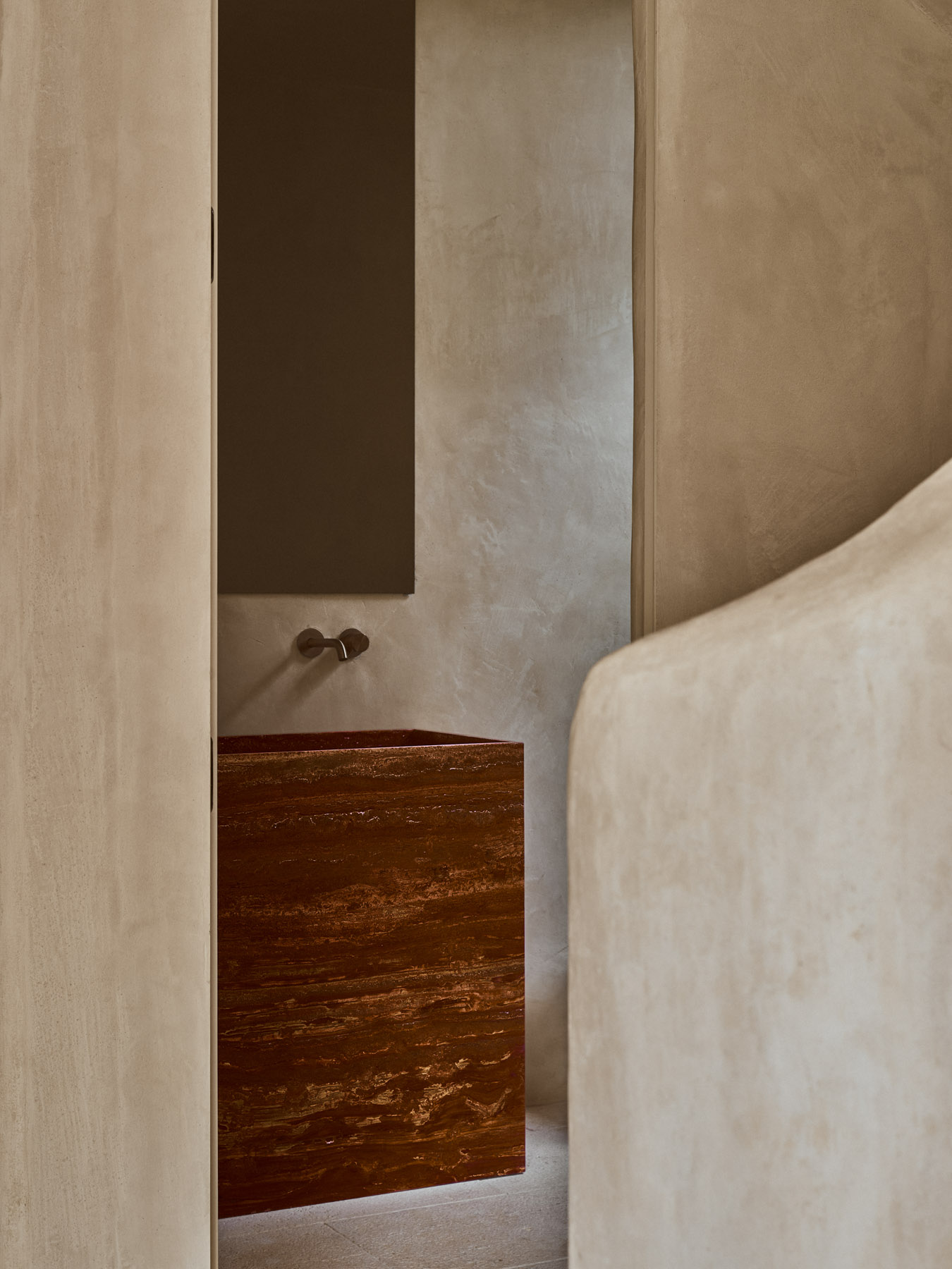 Minimal bathroom detail with natural stone basin and textured plaster walls.