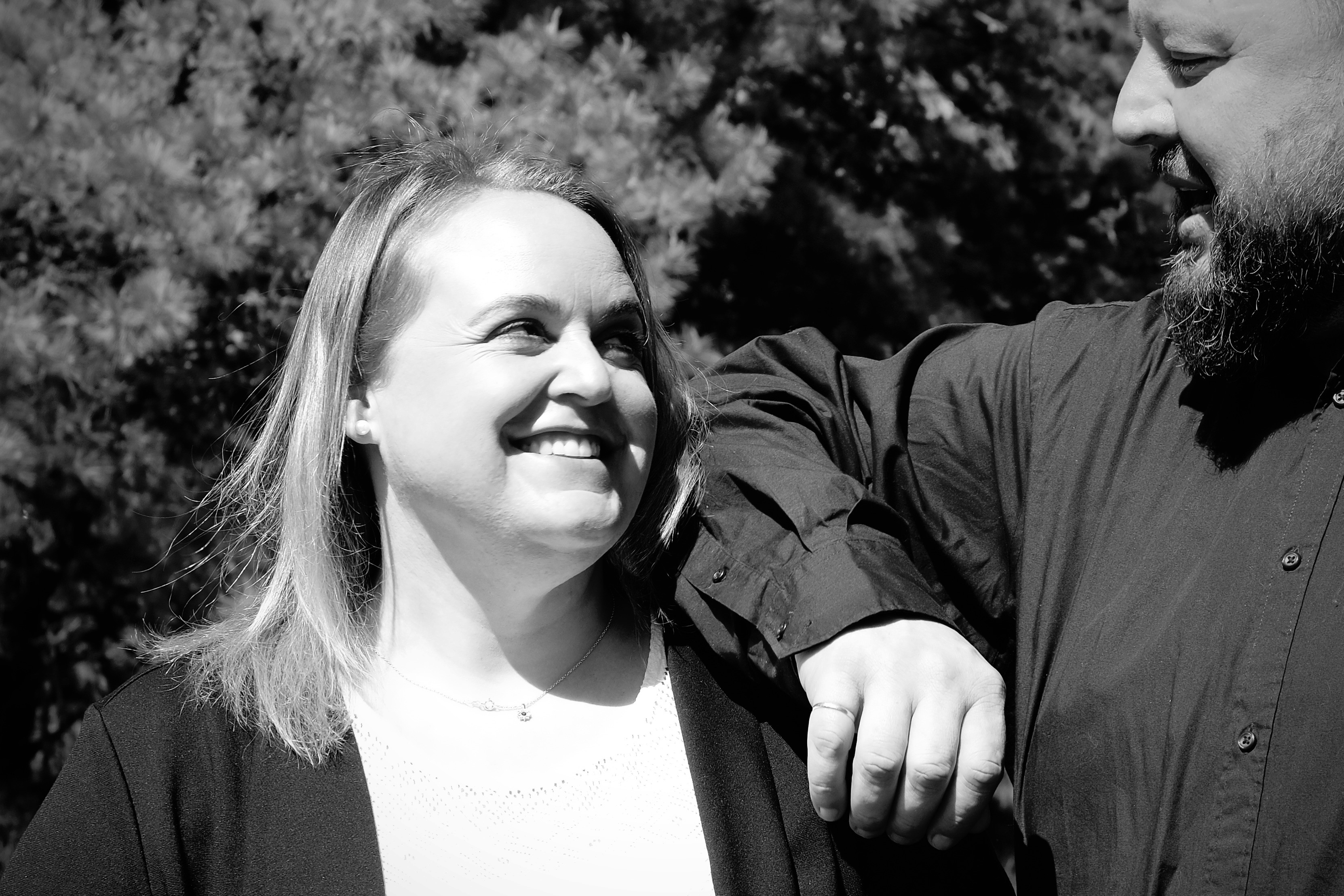 A woman lying down on a soft surface with her eyes closed, bathed in warm sunlight filtering through leaves. Her face has a natural glow, reflecting relaxation and tranquility in a serene spa-like setting.