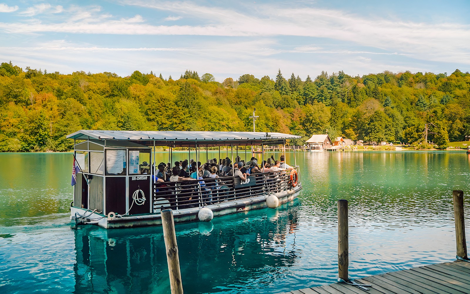 Boat tour on Plitvice Lakes with passengers enjoying scenic views of lush forests.