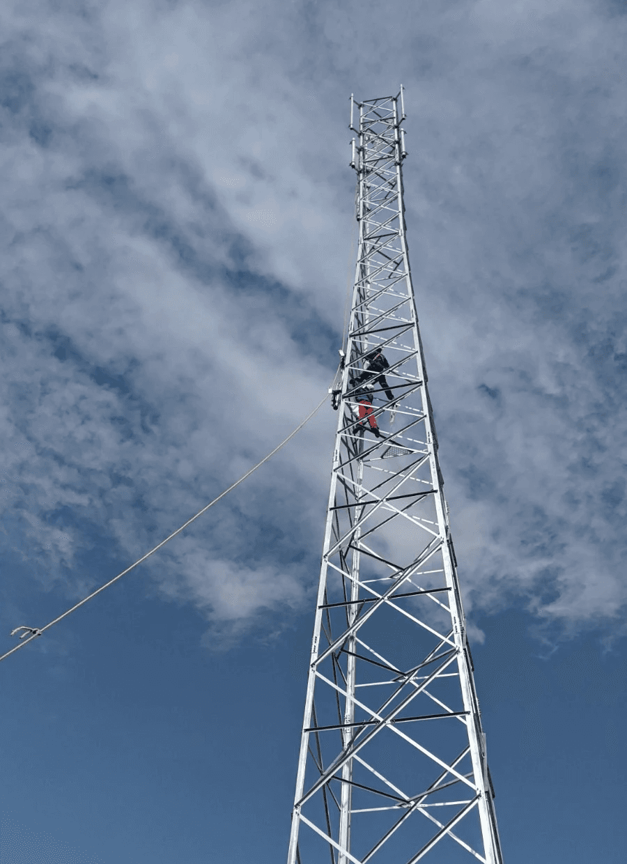 Smiling young woman with long hair standing against a dark green background, holding a finger to her chin.