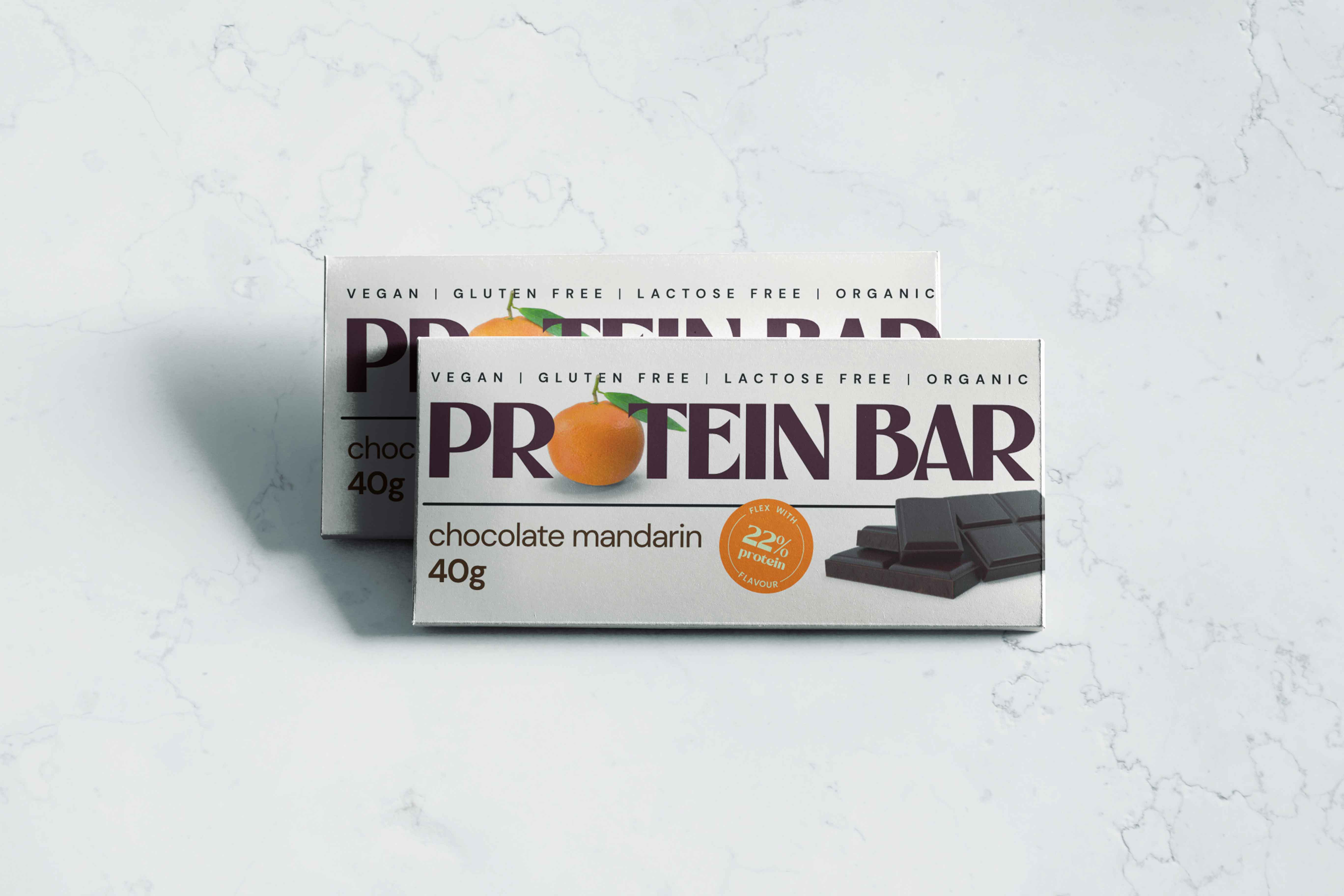 Chocolate chip protein bar on a counter with "Dubai Dates Nutrition" text. The bar is labeled "Vegan, Gluten-Free, Lactose-Free, Organic, 40g Protein, Chocolate Mandarin".