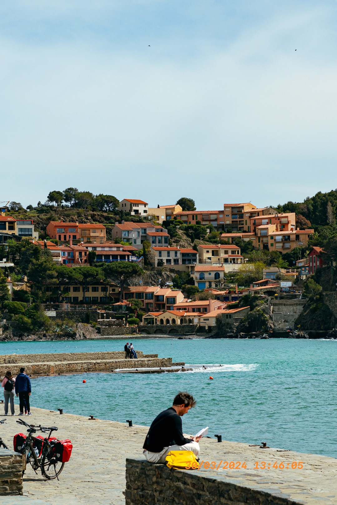 Homme lisant sur la jetée avec vue sur les maisons colorées de Collioure.