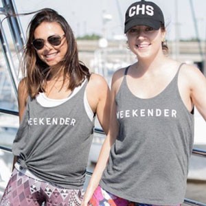 Two women wearing "Weekender" tank tops, smiling on a boat.