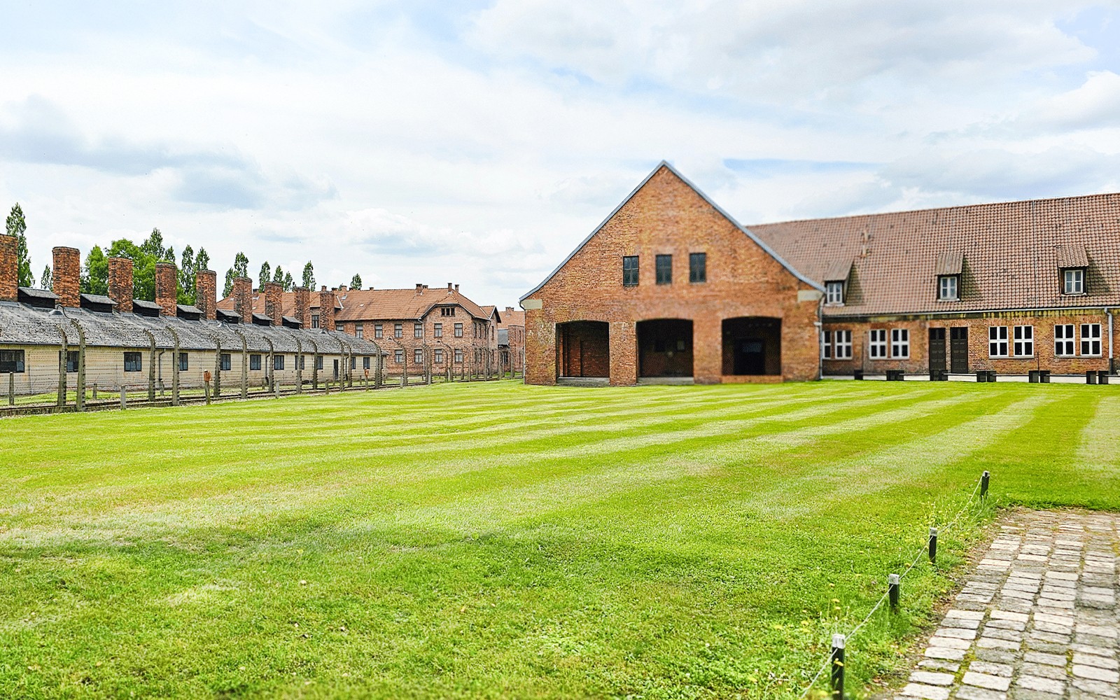 Barracones de Auschwitz Birkenau y el edificio principal con césped verde en primer plano.
