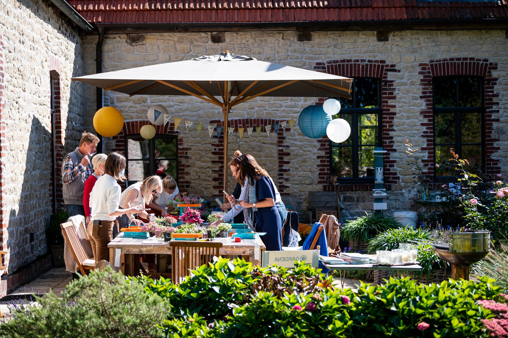 Im Freien, unter Sonnenschirmen, bepflanzen die Workshopteilnehmenden bei Gardena ihre individuellen Gefäße.