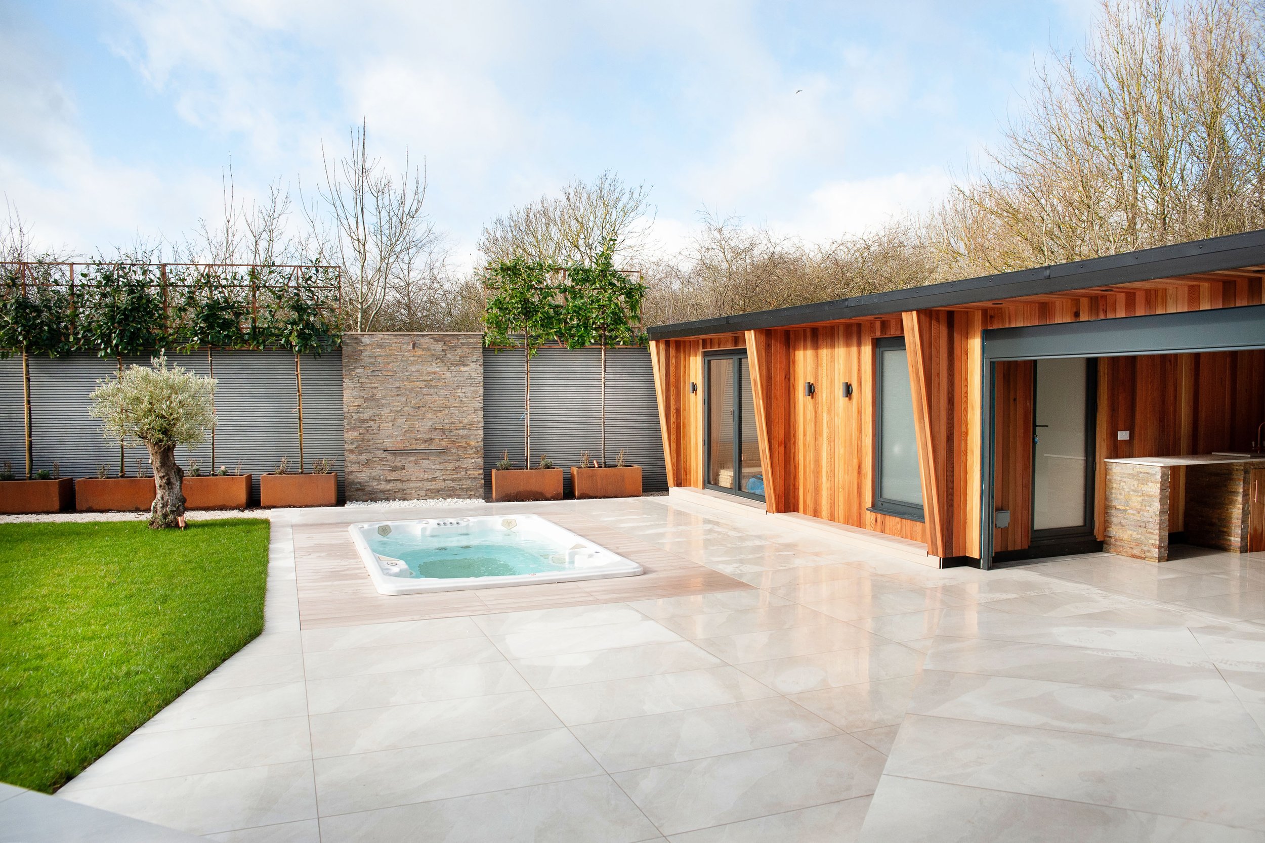 A modern outdoor space featuring a small pool, green grass, and wooden structures under a clear sky.