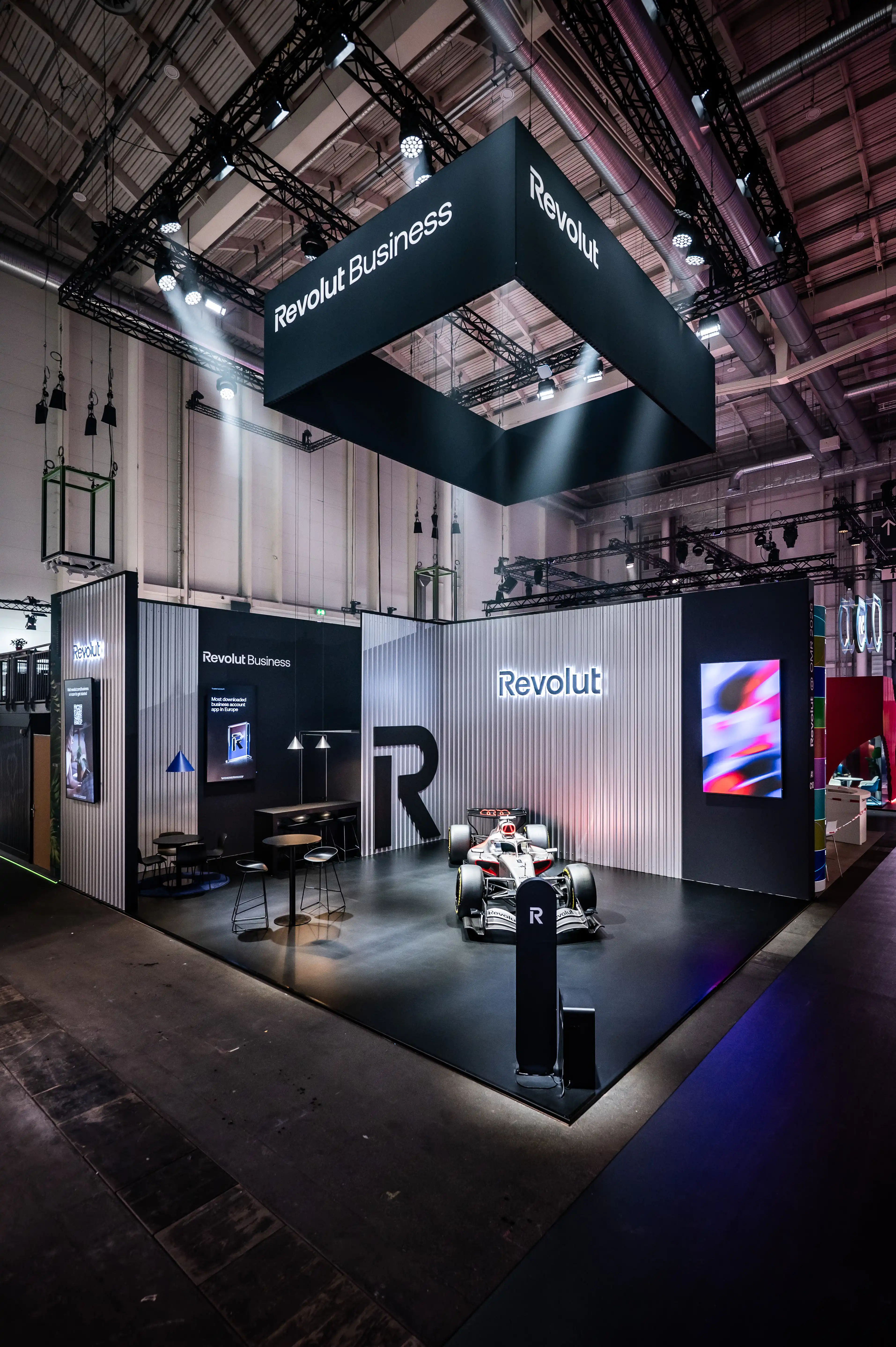 Overview of the Revolut booth with black hanging banner, Formula 1 car and silver corrugated facade.