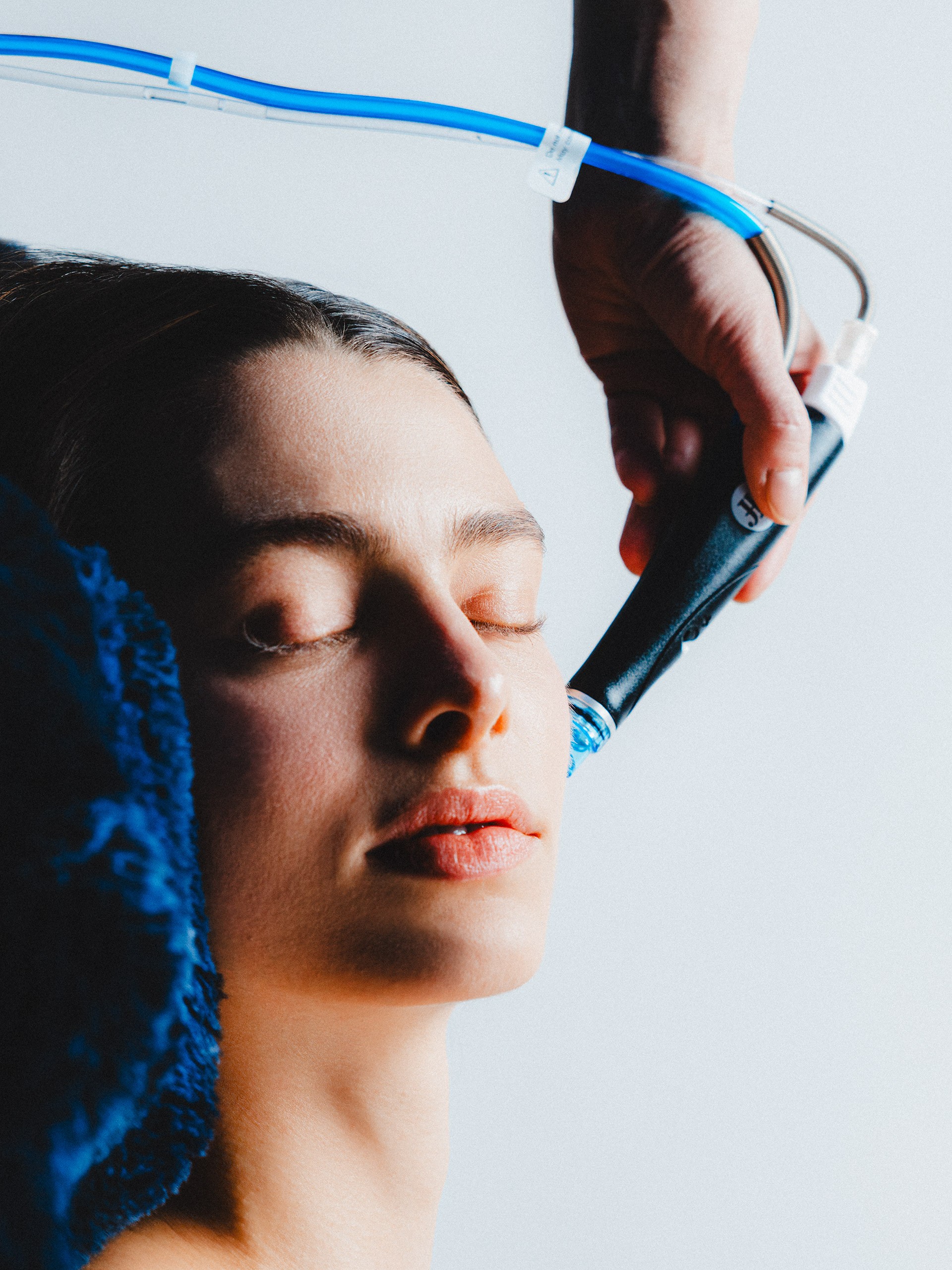 Woman receiving skincare treatment with a blue-handled device for facial rejuvenation.