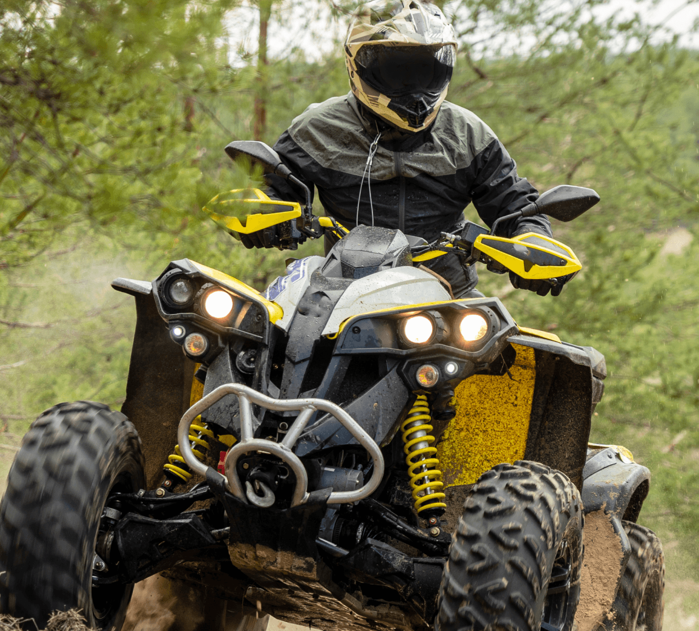 Person riding an ATV through a forest trail, matching the yellow and black brand accents