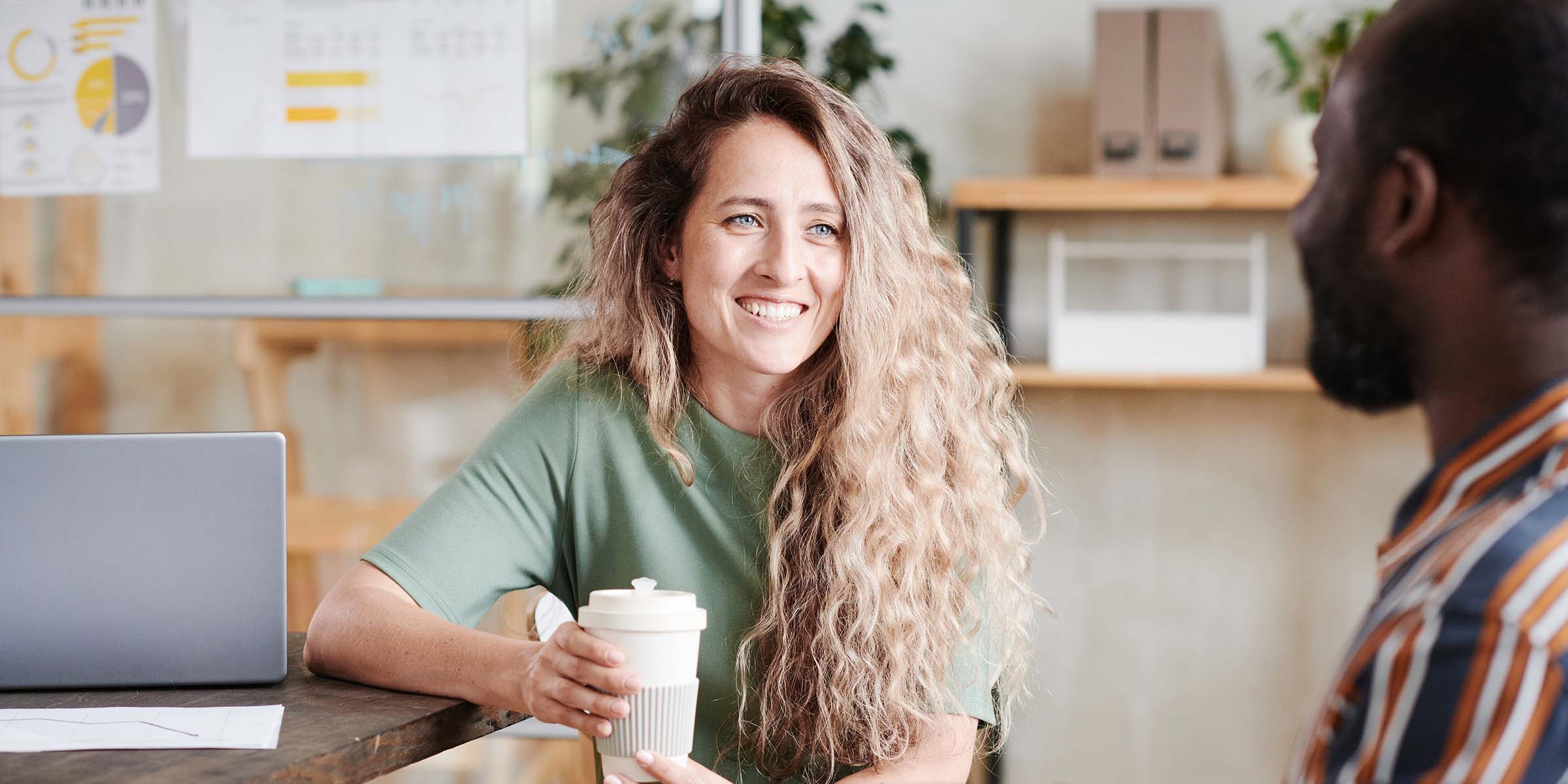 Woman sat with a laptop next to her, chatting to man, smiling and happy