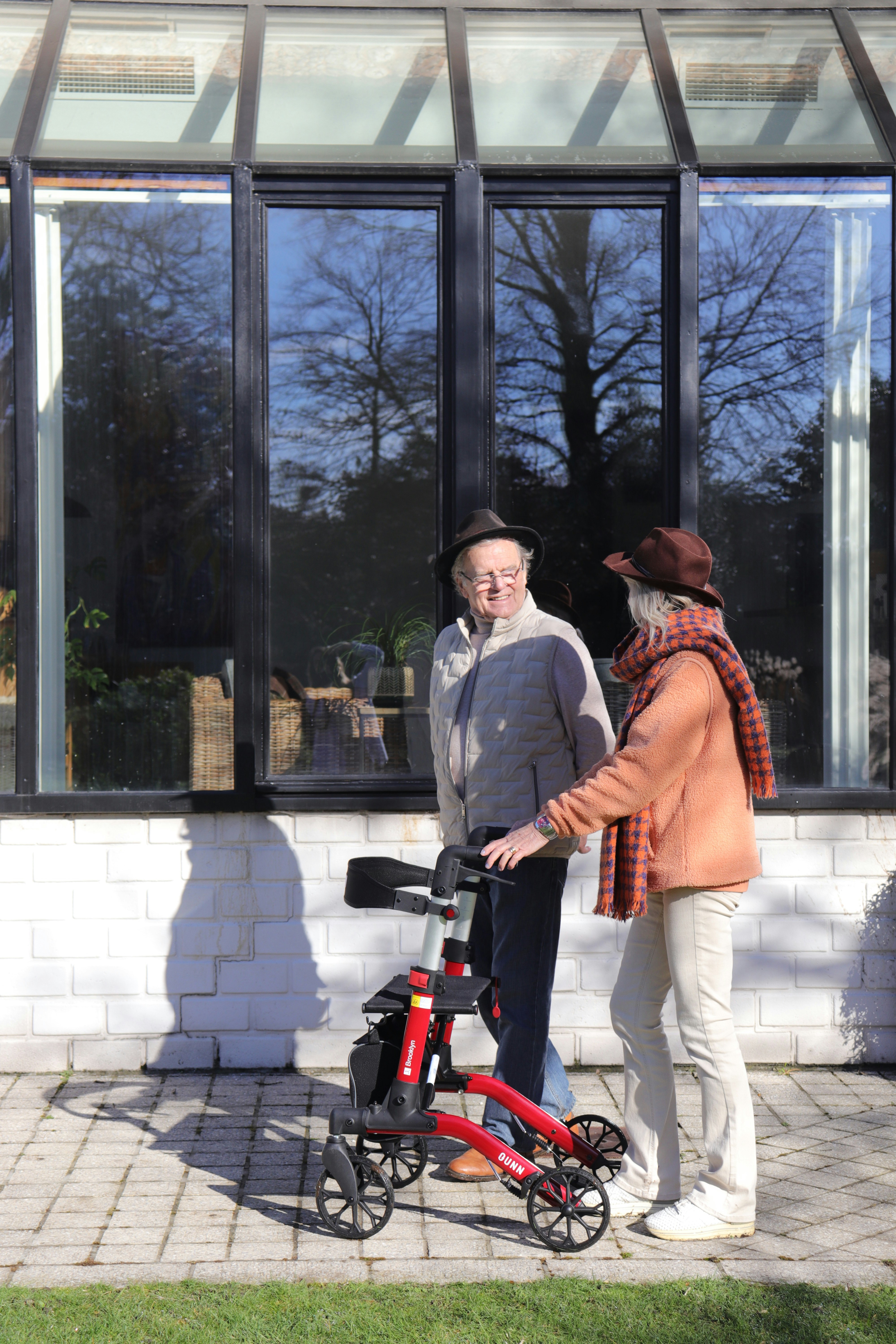 Elderly couple with a red walker outside.