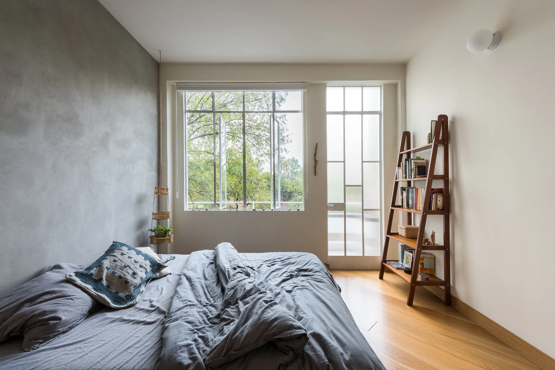 Recámara con muro de concreto, ventanales al exterior y escalera-librero de madera