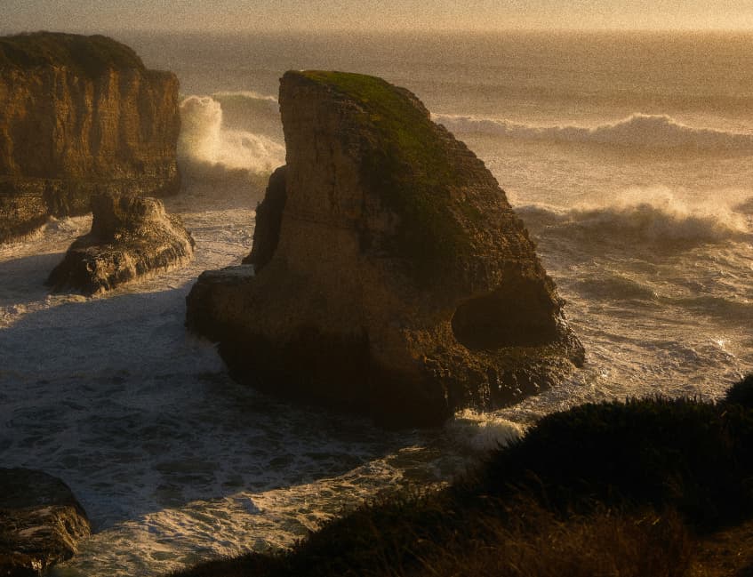 Waves crash against rocky coastal formations at sunset.