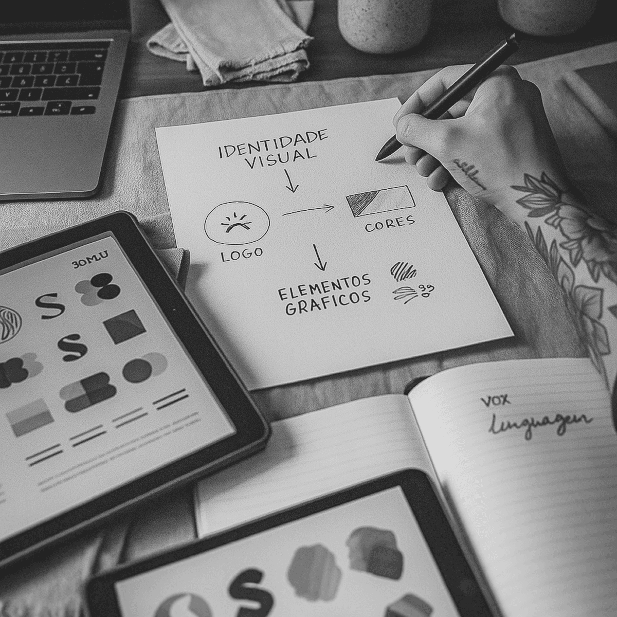 Elementos gráficos e papel com esboços de logotipo sobre mesa clara, ilustrando o desenvolvimento de identidade visual com foco em originalidade e precisão