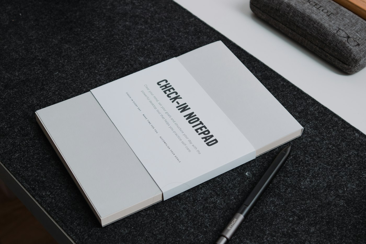 A closed notebook and pen on a dark felt desk mat