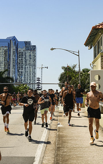Group of runners participating in a community fitness run along the Miami streets, with modern high-rise buildings and palm trees in the background