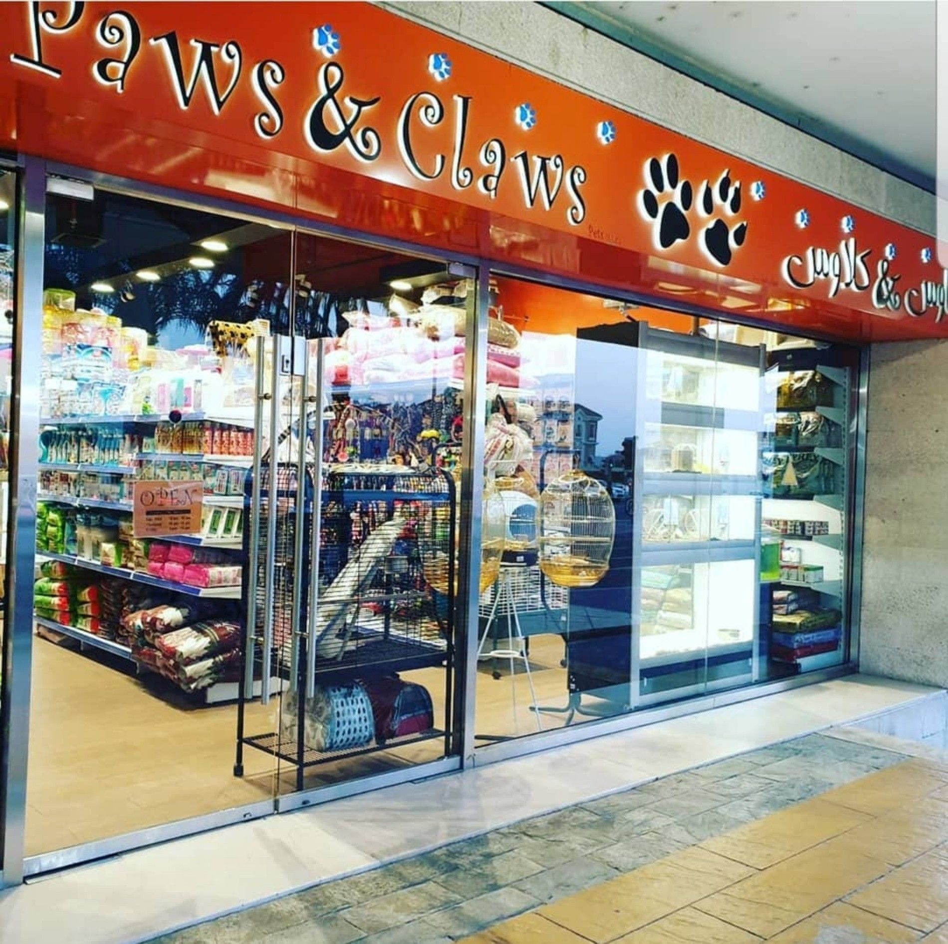 The exterior view of Paws & Claws Pets with glass windows, double glass doors, and shelves full of pet food and other products.