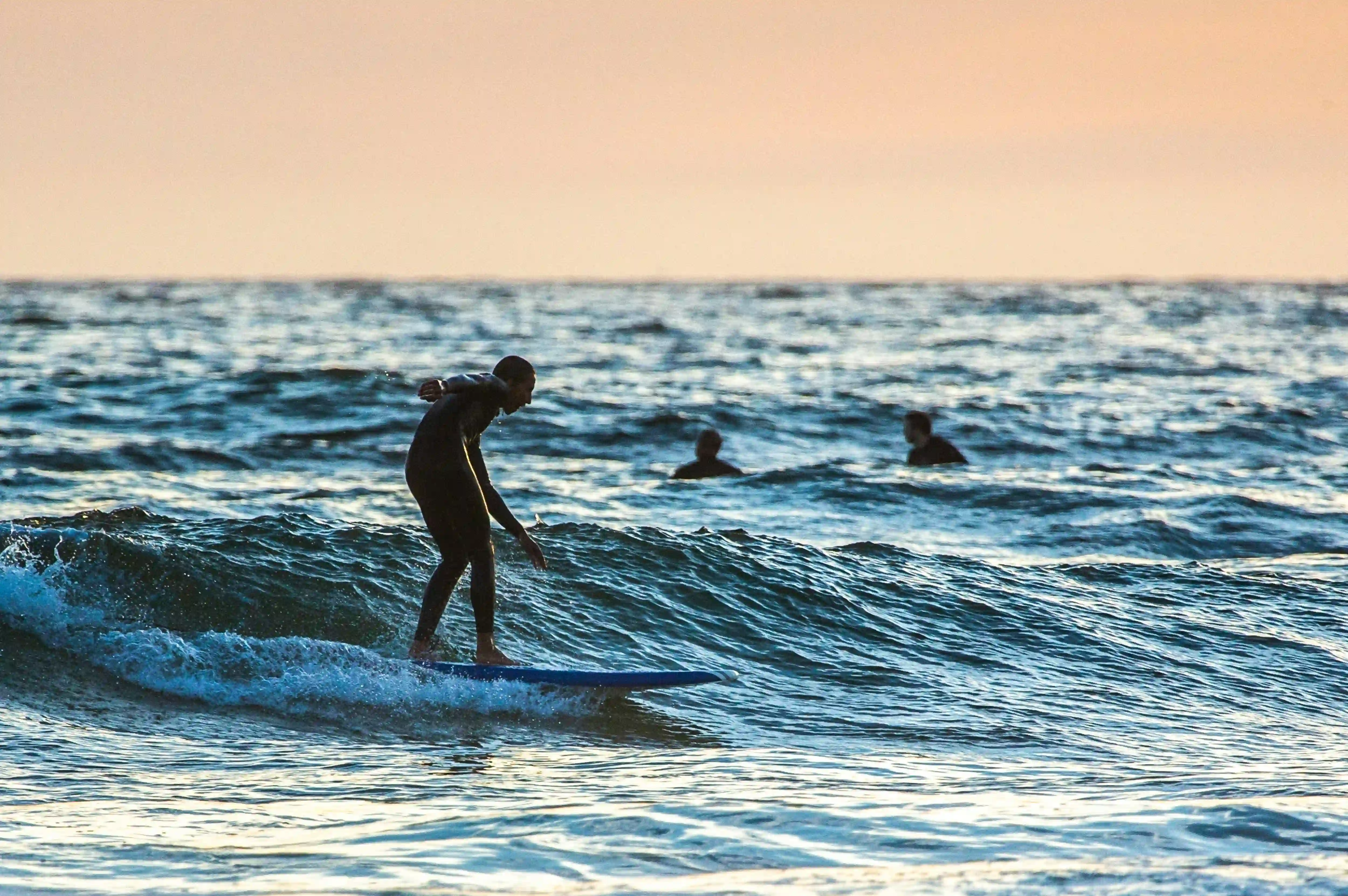 Surfer riding a small wave at sunset with other surfers waiting in the background.