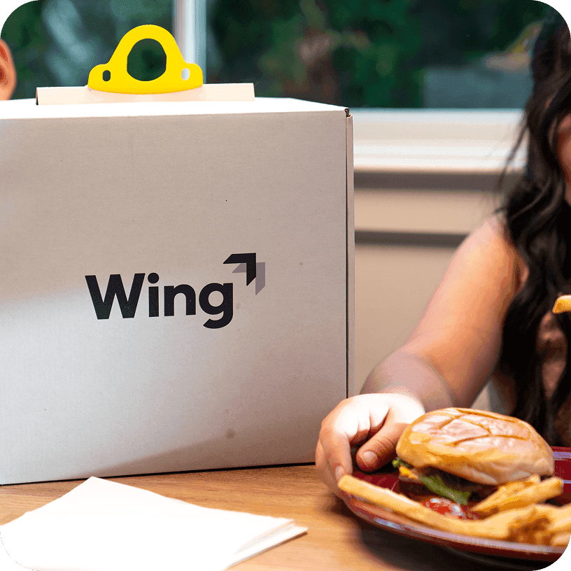A person in a red uniform places a packaged sushi tray on a counter beside a branded DoorDash delivery container, highlighting food delivery services.