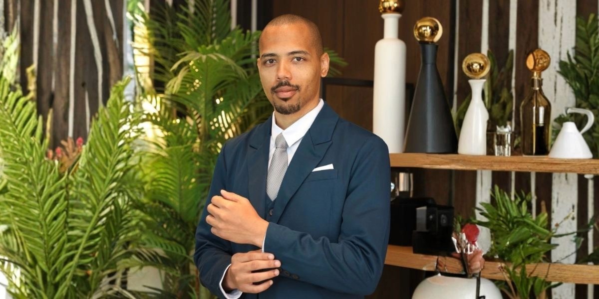 Wilme Ulasia dressed in a tailored suit, presenting a professional image amidst lush greenery.