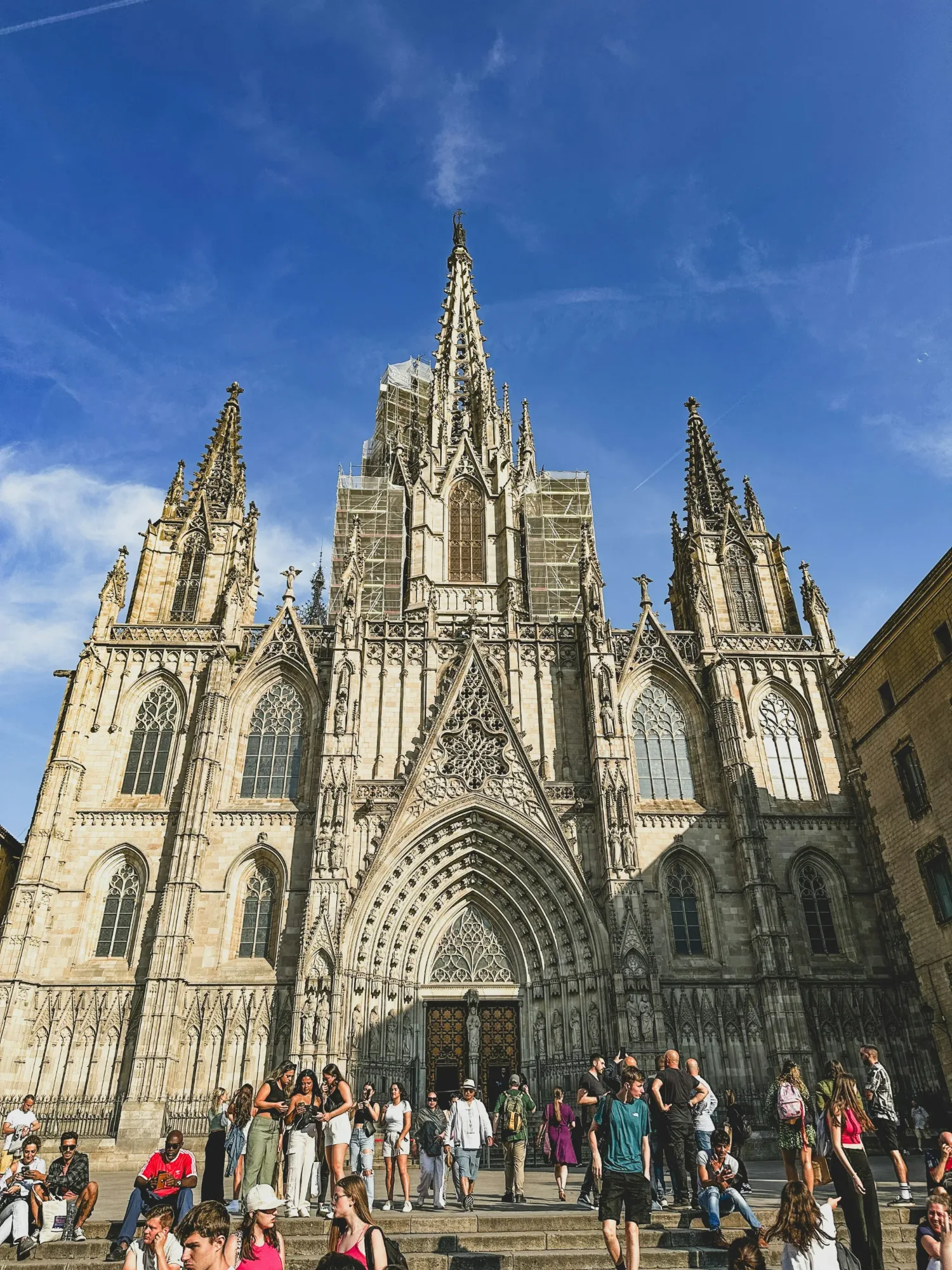 Gothic architecture of Barcelona Cathedral, Spain, with tourists admiring the facade on a sunny day.