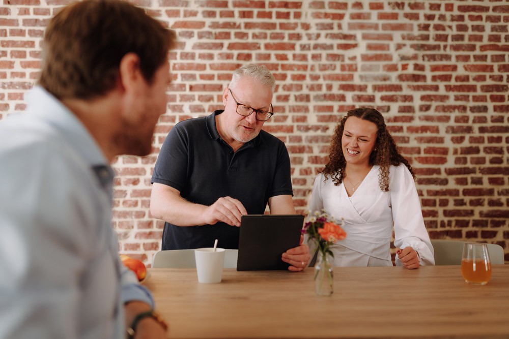Drei Personen stehen vor einer Backsteinwand an einem Tisch und führen ein Gespräch.