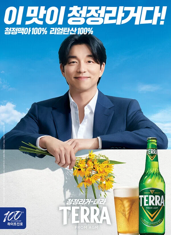 Actor Gong-yoo smiles in a suit holding yellow flowers; in the foreground a glass and bottle of Terra beer