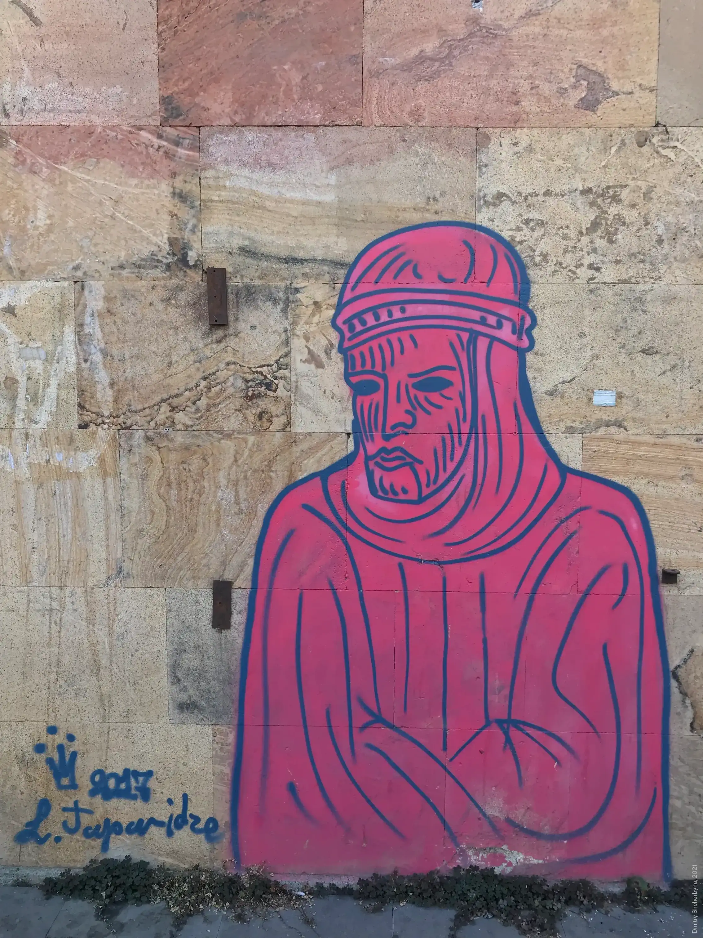 A stencil-style mural, in hot pink with dark blue outlines, on a sandstone wall shows the bust of a medieval figure wearing a banded helmet and robes with arms crossed.
