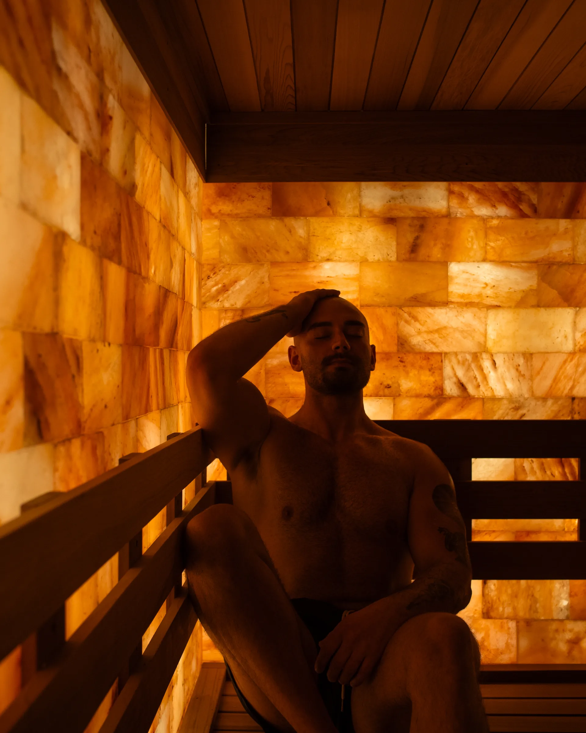 Person seated in a warm Himalayan salt sauna in Vancouver, lit by soft amber light.