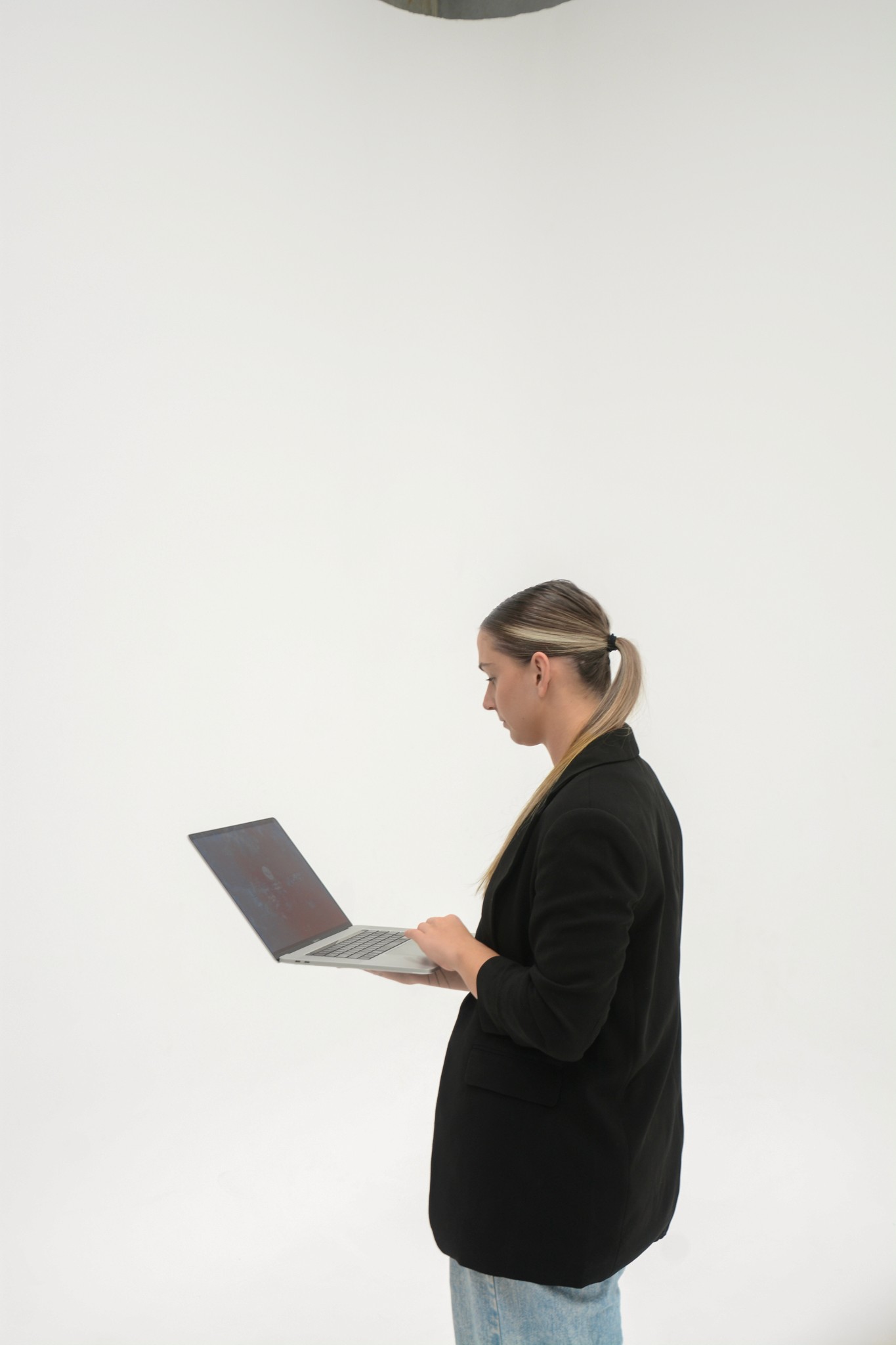 Modern minimalist desk setup with a computer monitor, microphone arm, camera, and indoor plants, featuring a pegboard with accessories on the wall and a Bauhaus-style poster leaning against the wall.