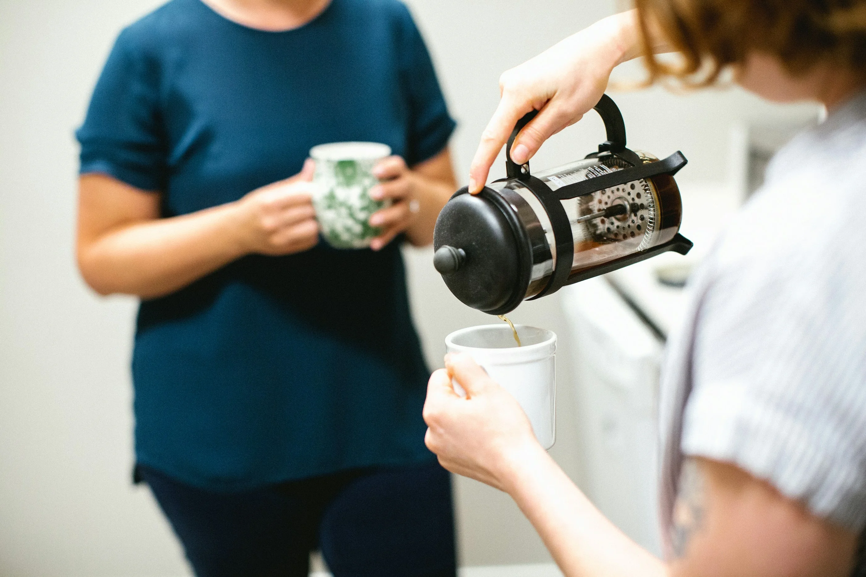 A volunteer pouring coffee from a French press into a guest’s mug