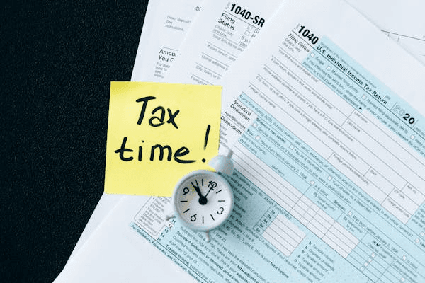 Tax forms with a clock and a sticky note reading 'Tax time!'