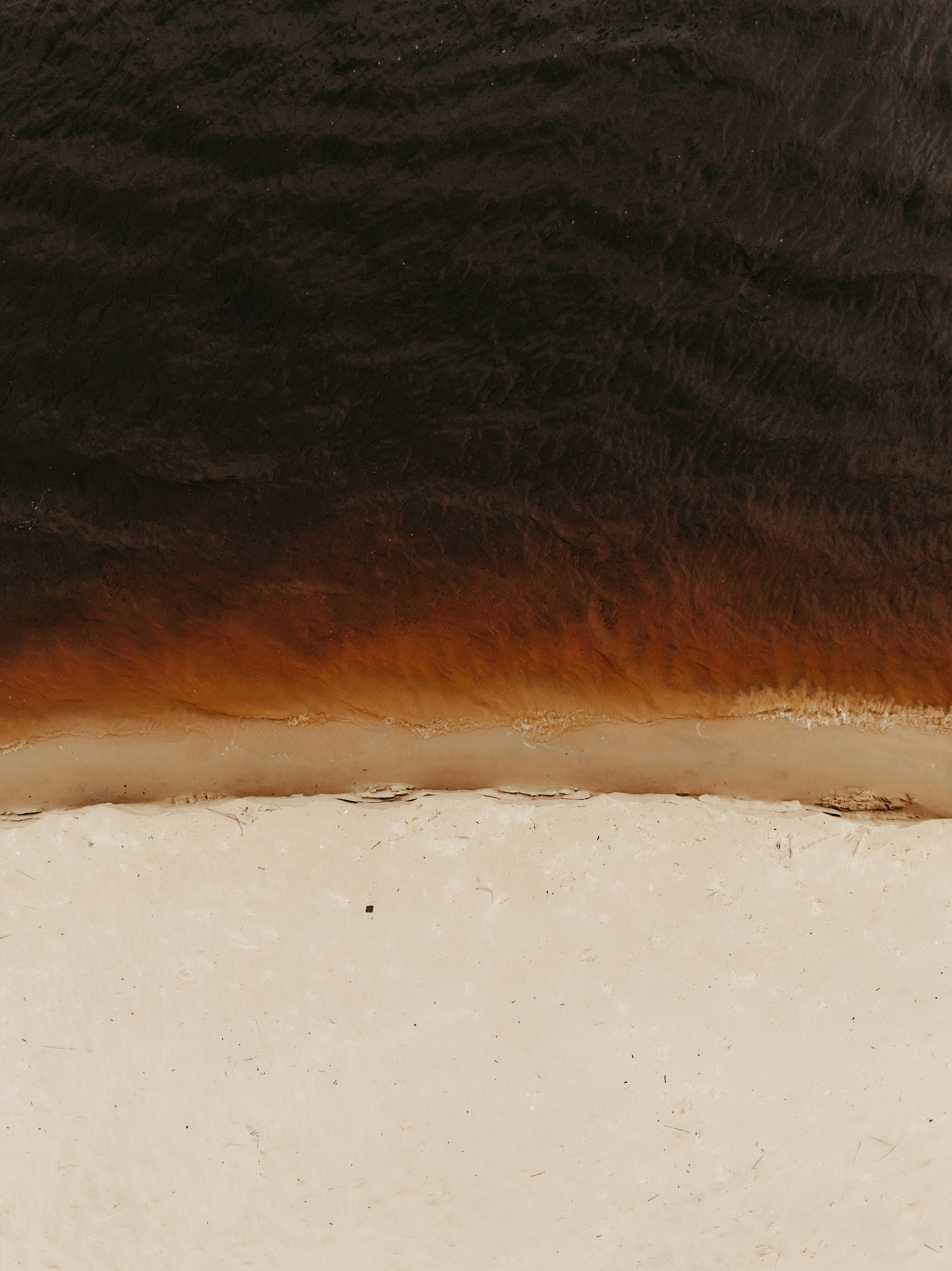 Dark water meets a sandy shore from above