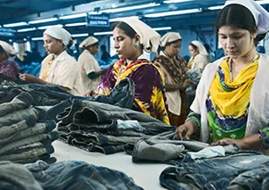 In a table full of finished denim pants factory multiple workers are checking the final finishing of those garment to ensure qualiy