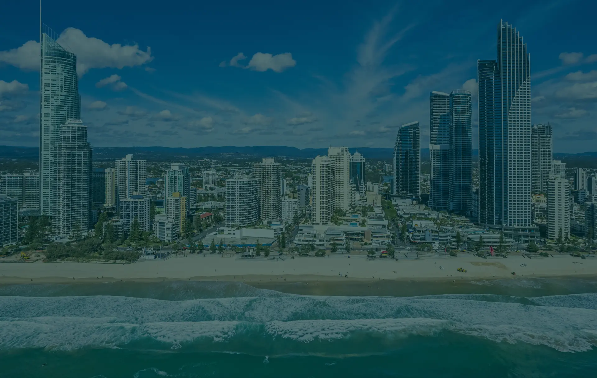 High-rise buildings line a beach with ocean waves.