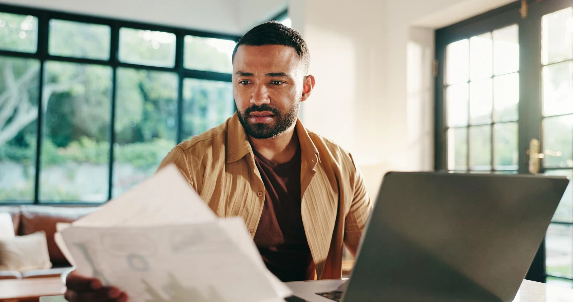 Man documents and home with laptop for financial statistics report or performance review Male person freelancer or remote wor
