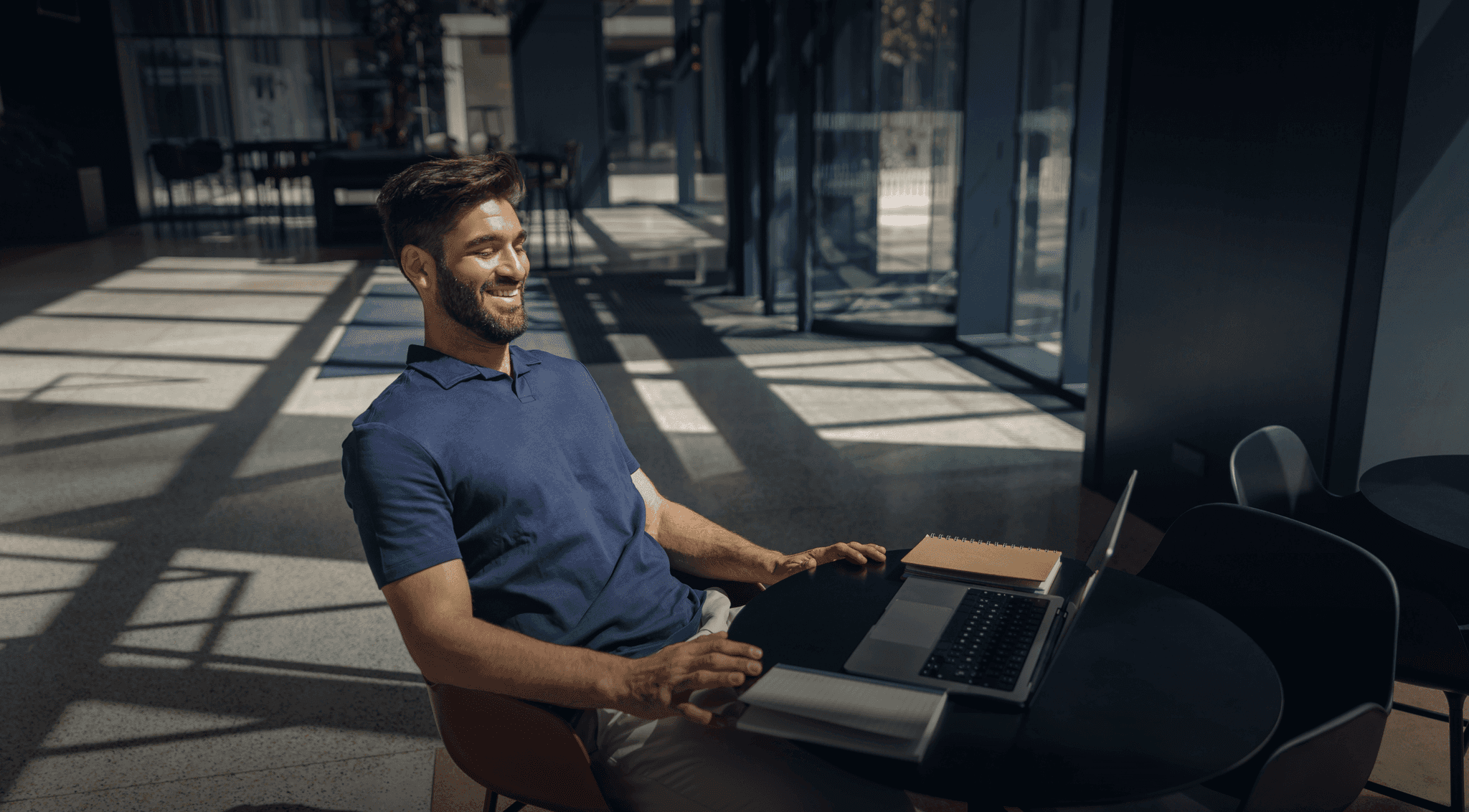 A young handsome man sitting at the table on his laptop wearing a blue shirt