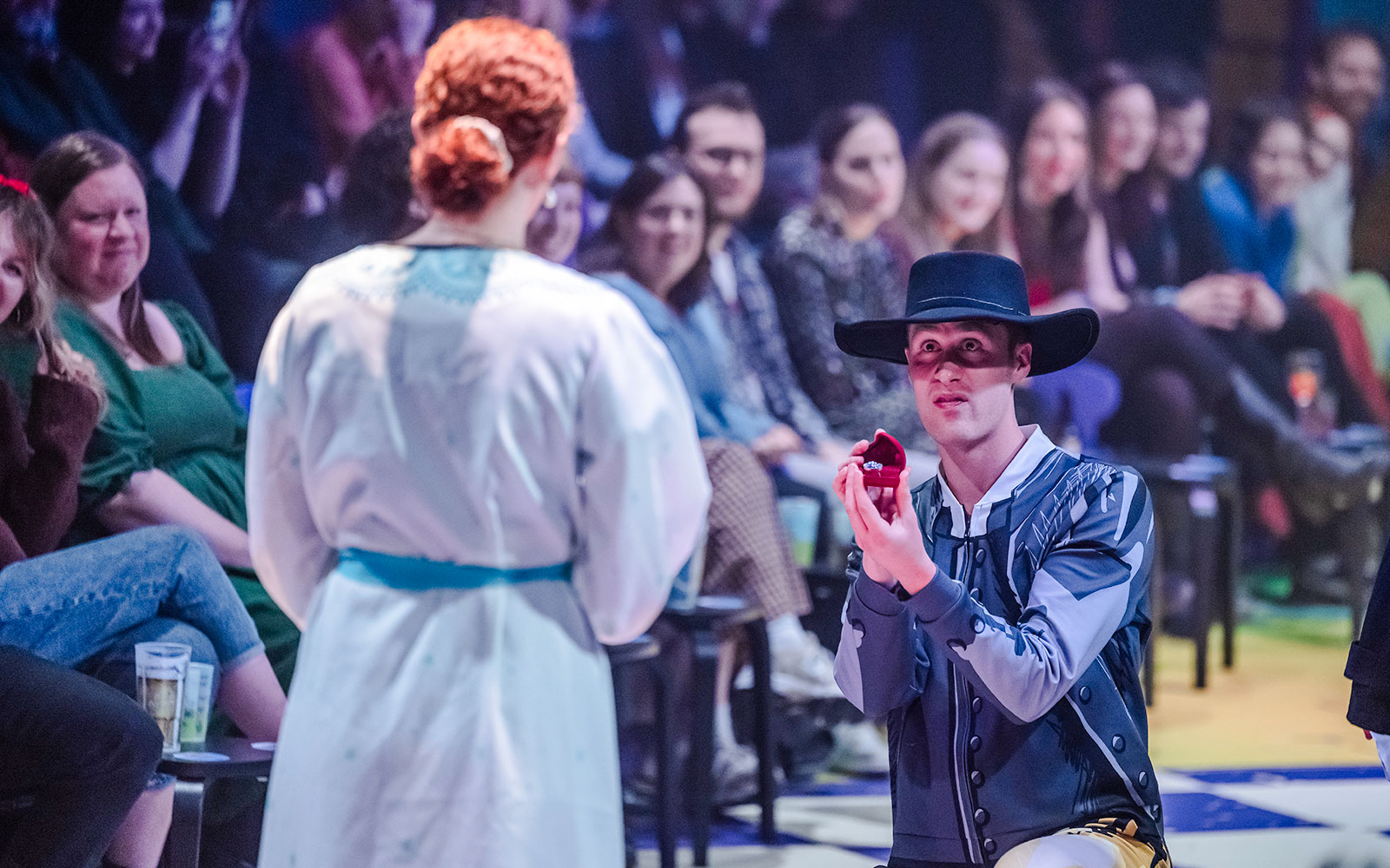 在“骄傲与偏见”演出中，一位穿着戏服的男士单膝下跪，呈上戒指盒。