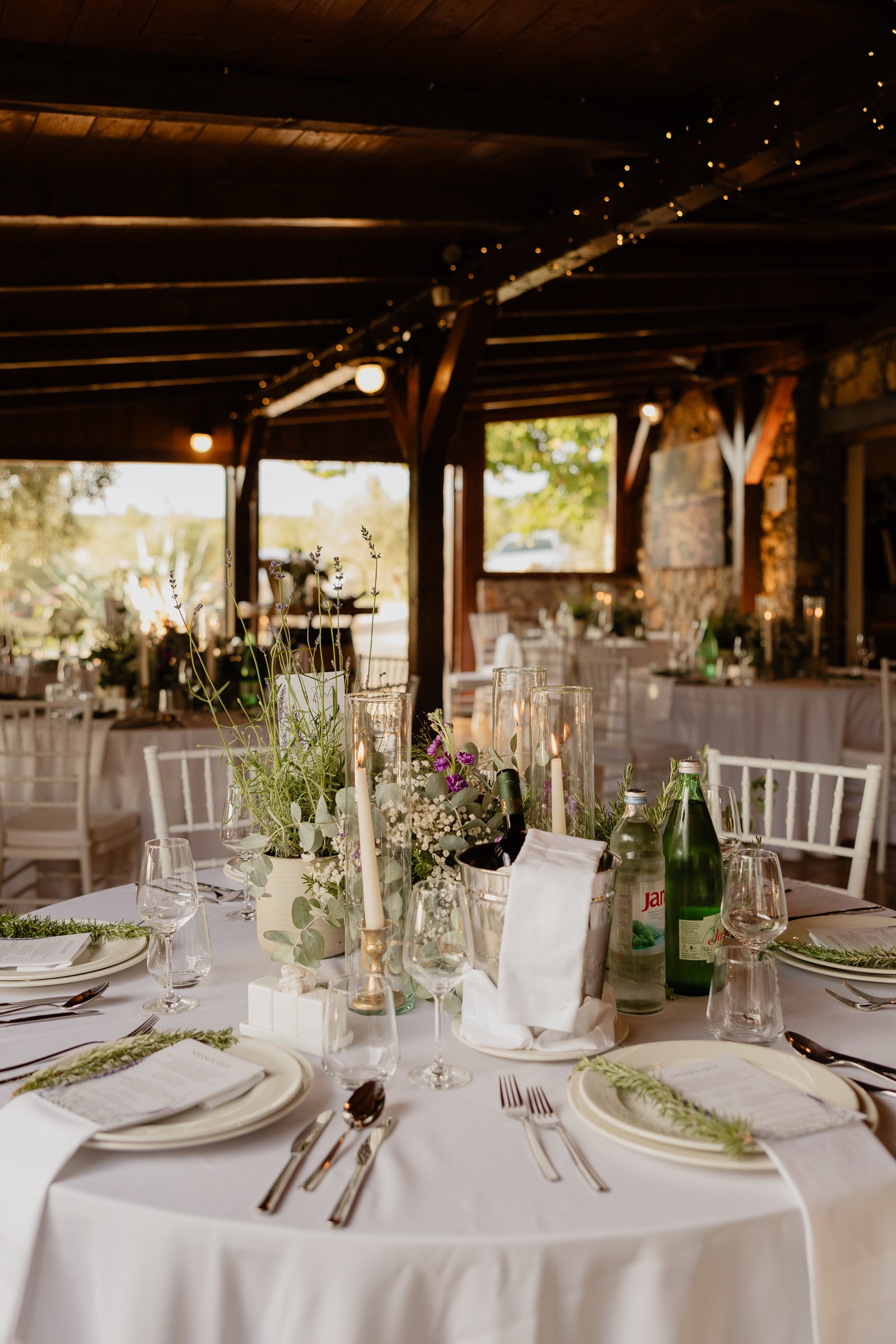 Wedding venue dining table with flower arrangement and plates with herbs, in a cosy rustic semi-outside space with wooden beams and stone walls