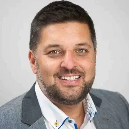 Confident woman with long curly hair wearing sunglasses and a shimmering top, photographed from a low angle against a deep blue sky.