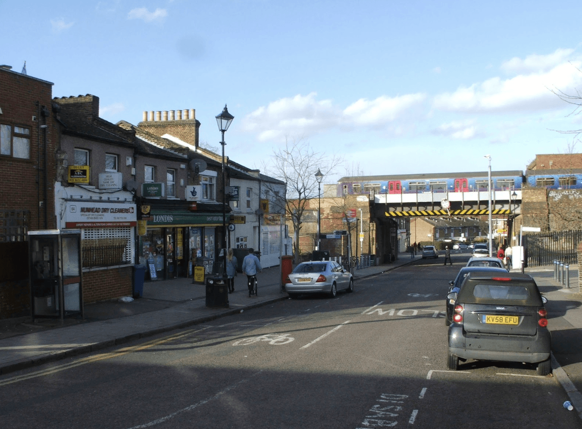 A smiling man with curly hair is sitting at a desk, looking at the camera, with a laptop and a lamp in the background.